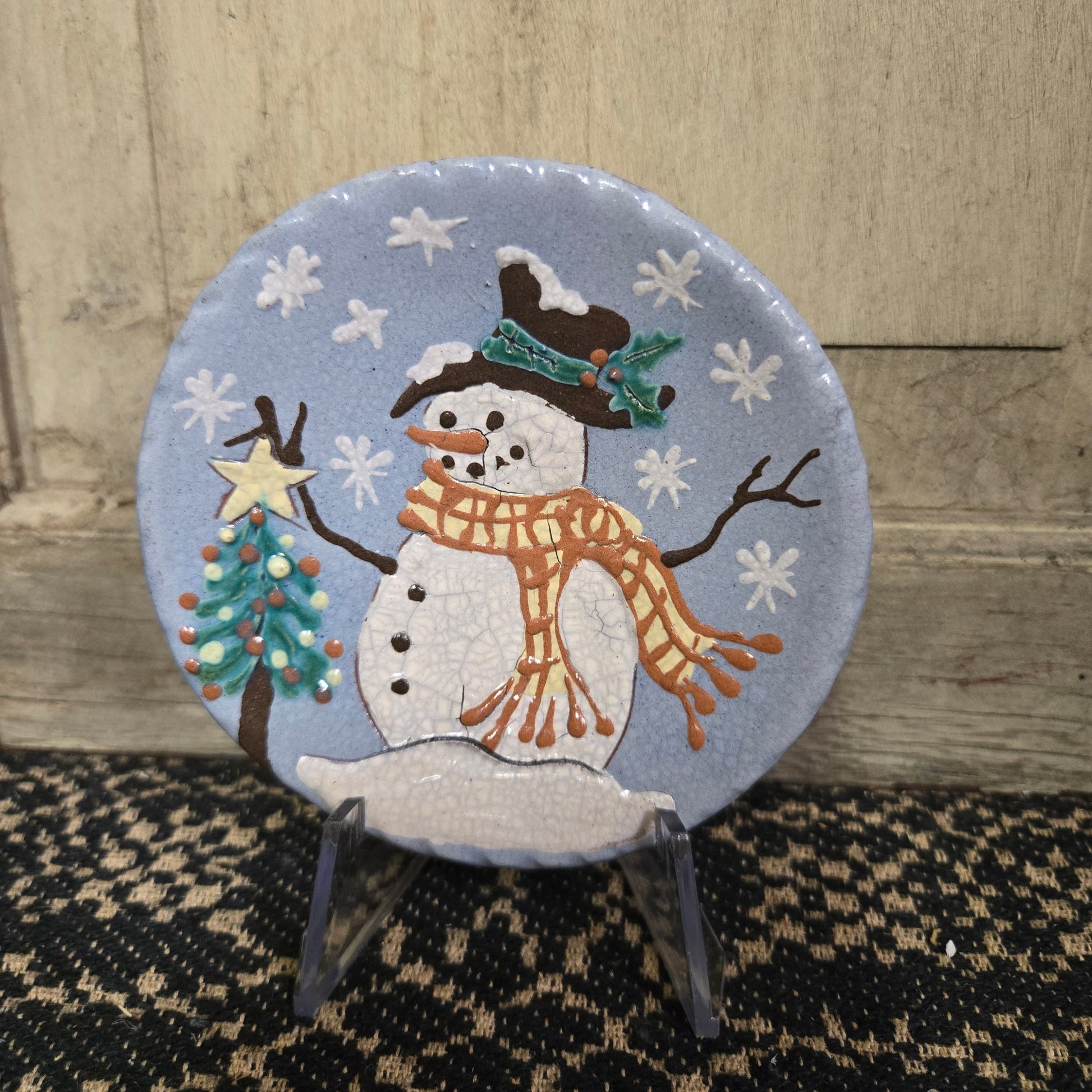 Vibrant blue redware plate with snowman putting a star on top of a Christmas tree