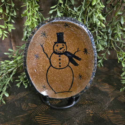 Decorative stoneware plate with a snowman design on a wooden surface with greenery