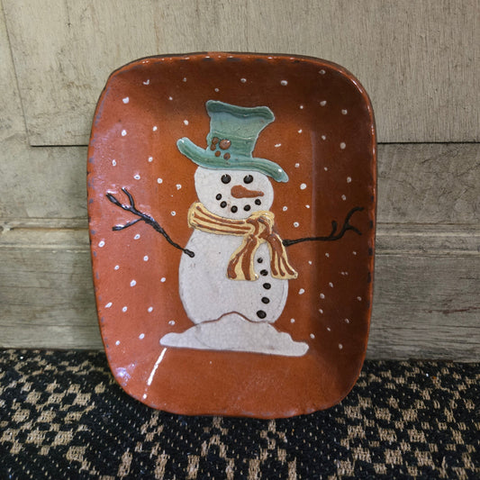 Small rectangular redware plate featuring a snowman with stick arms surrounded by flurries of snow