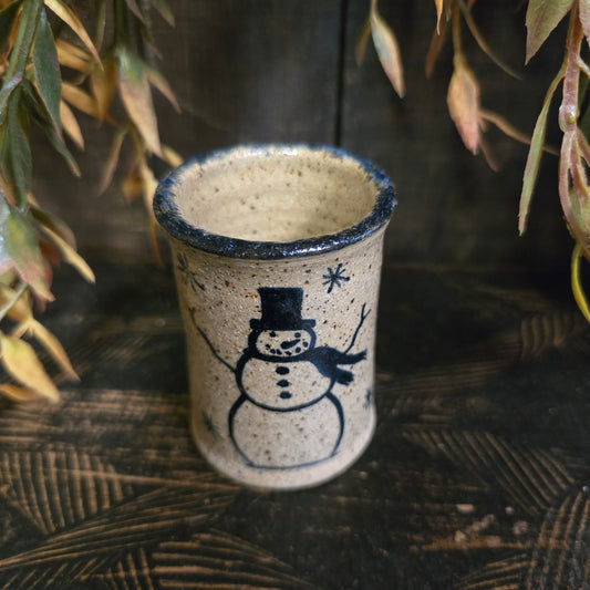 Ceramic cup with a snowman design on a wooden surface with plants.
