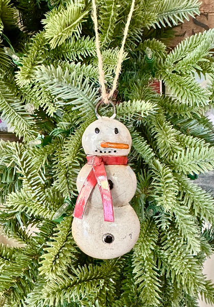 Decorative snowman ornament with a pink bow hanging on a Christmas tree.