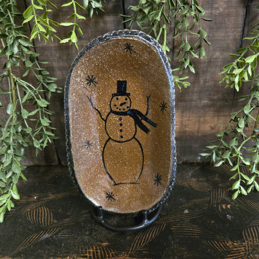 Decorative plate with a snowman design on a wooden surface with greenery