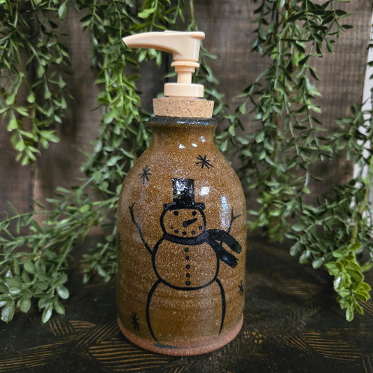 Decorative bottle with a snowman design on a wooden surface with greenery