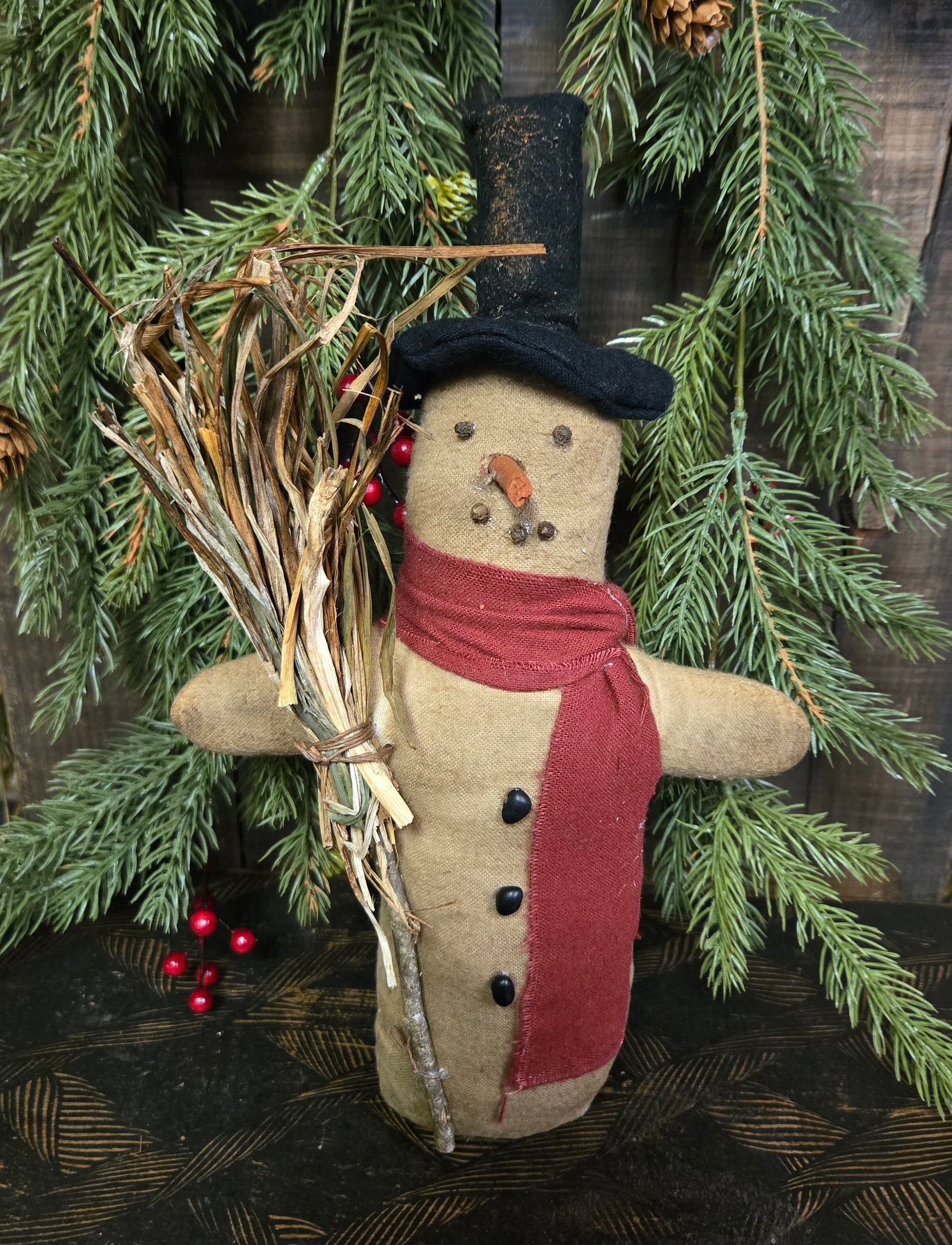 Textile snowman with a red scarf and top hat, surrounded by greenery