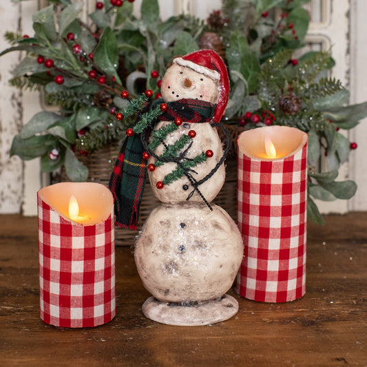 Snowman with pencil tree wearing red hat with checkered pillar candles and greenery.