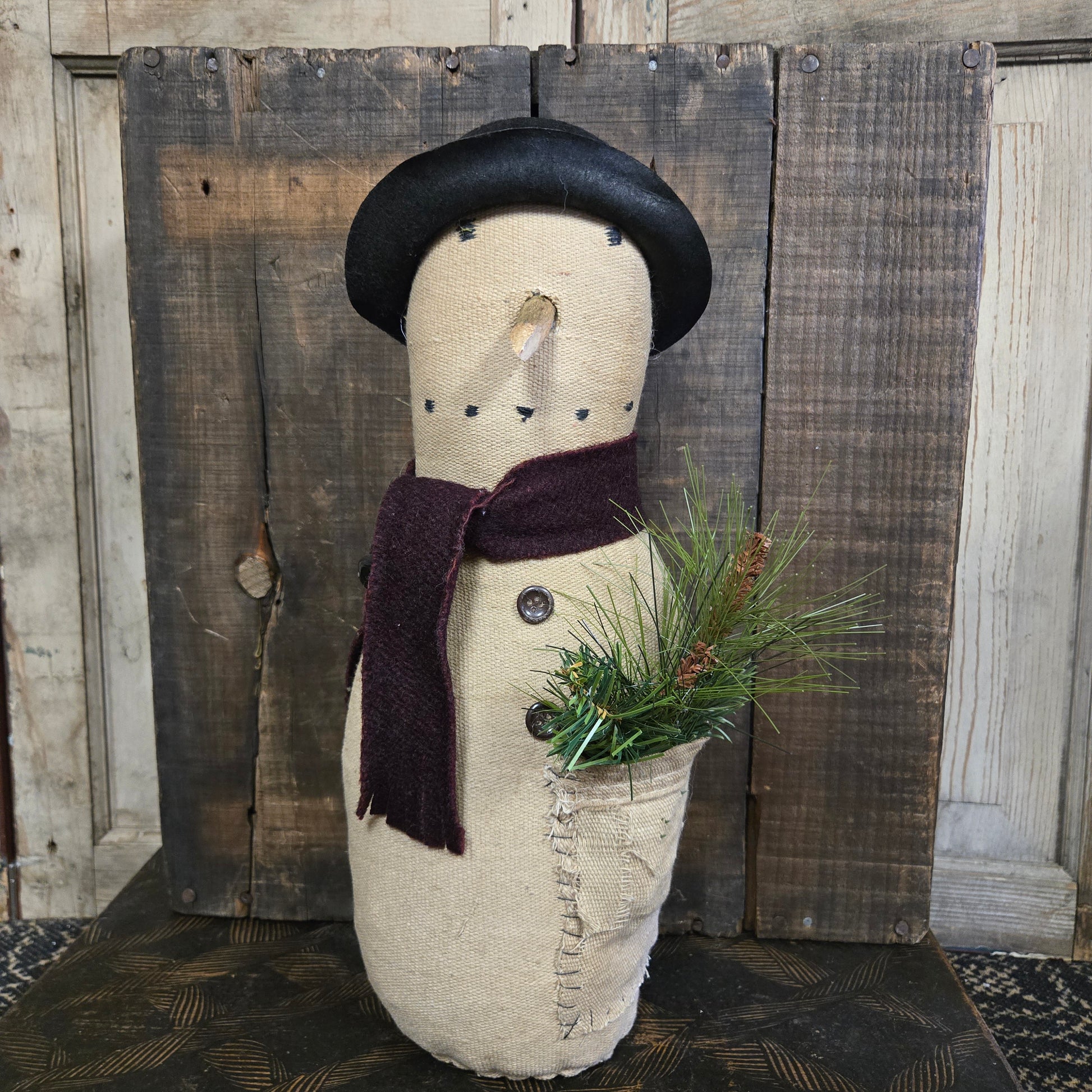 Decorative snowman figure with a black top hat and greenery on a wooden background