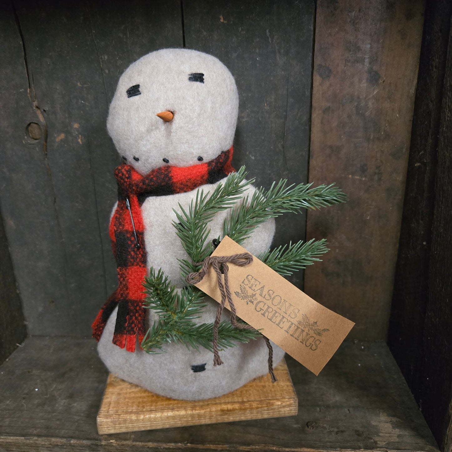 Decorative snowman with a plaid scarf and greenery on a rustic wooden surface.