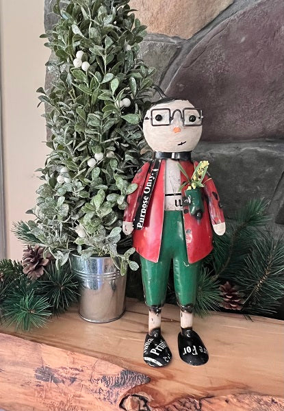 A decorative snowman figure with square glasses, wearing a red and green outfit, standing next to a artificial green plant.