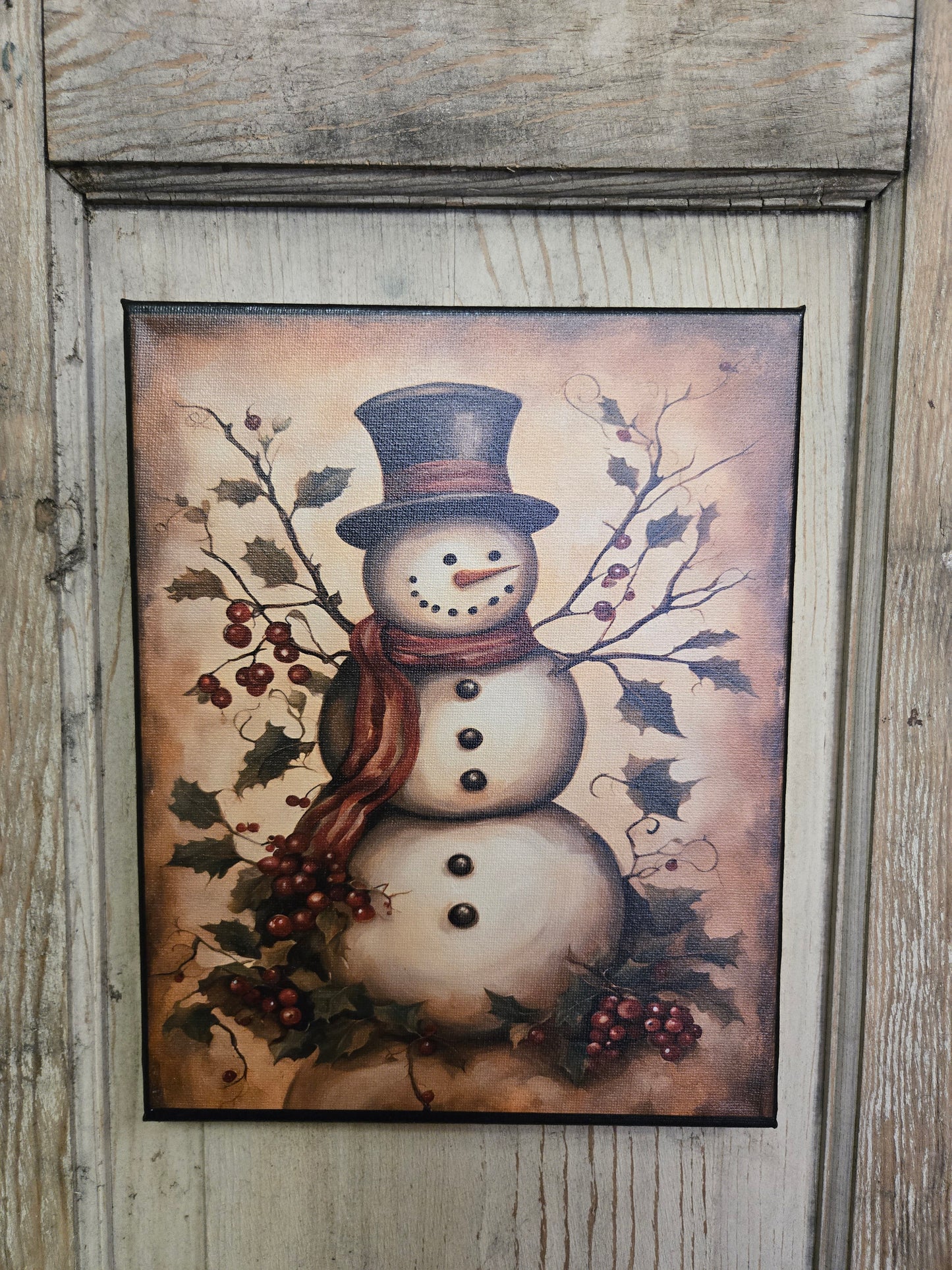 A canvas print featuring a snowman with a top hat and standing among berries, with a rustic wooden background.