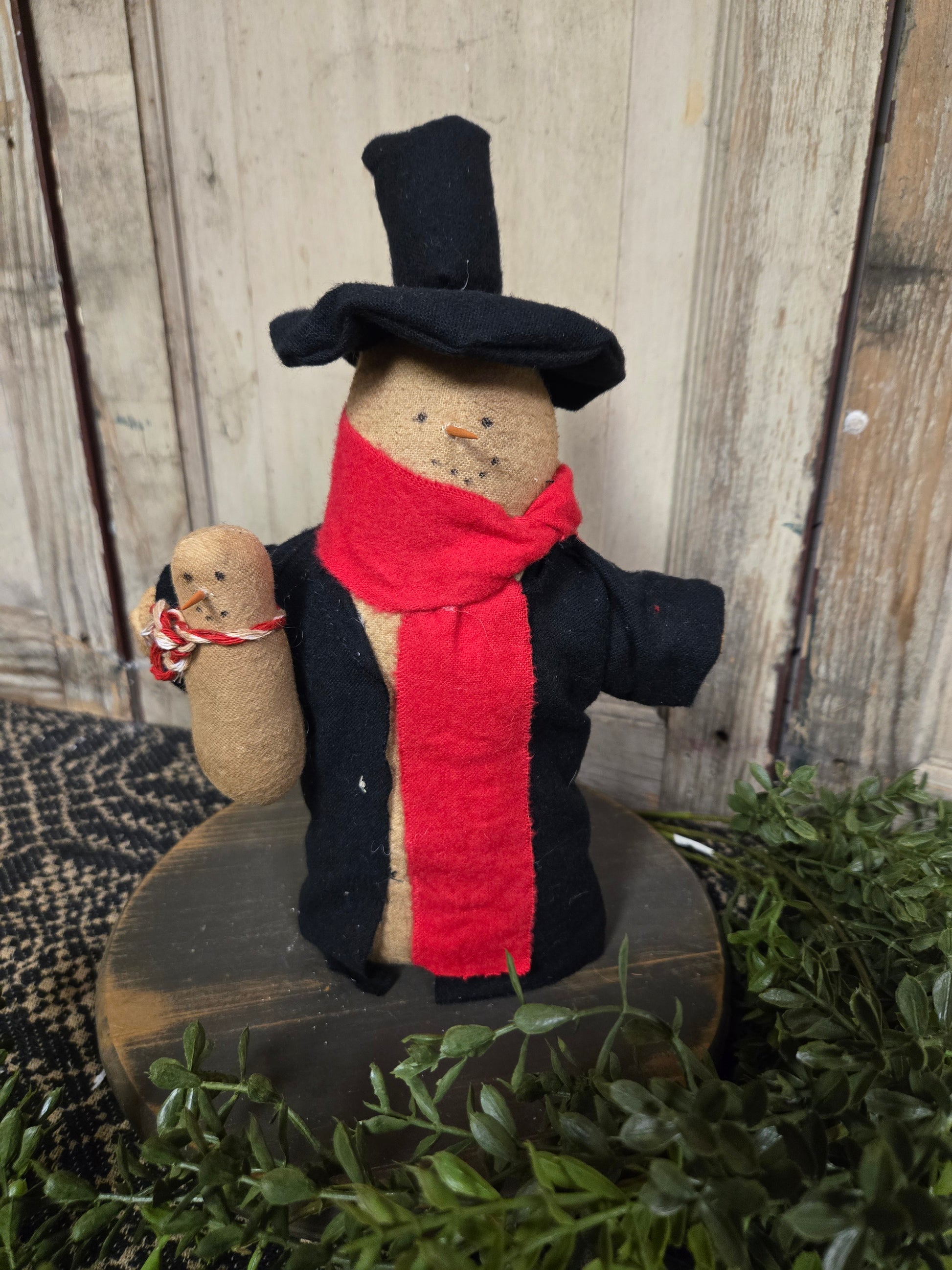 A handcrafted snowman with a top hat holding a baby snowman, both dressed in festive attire.