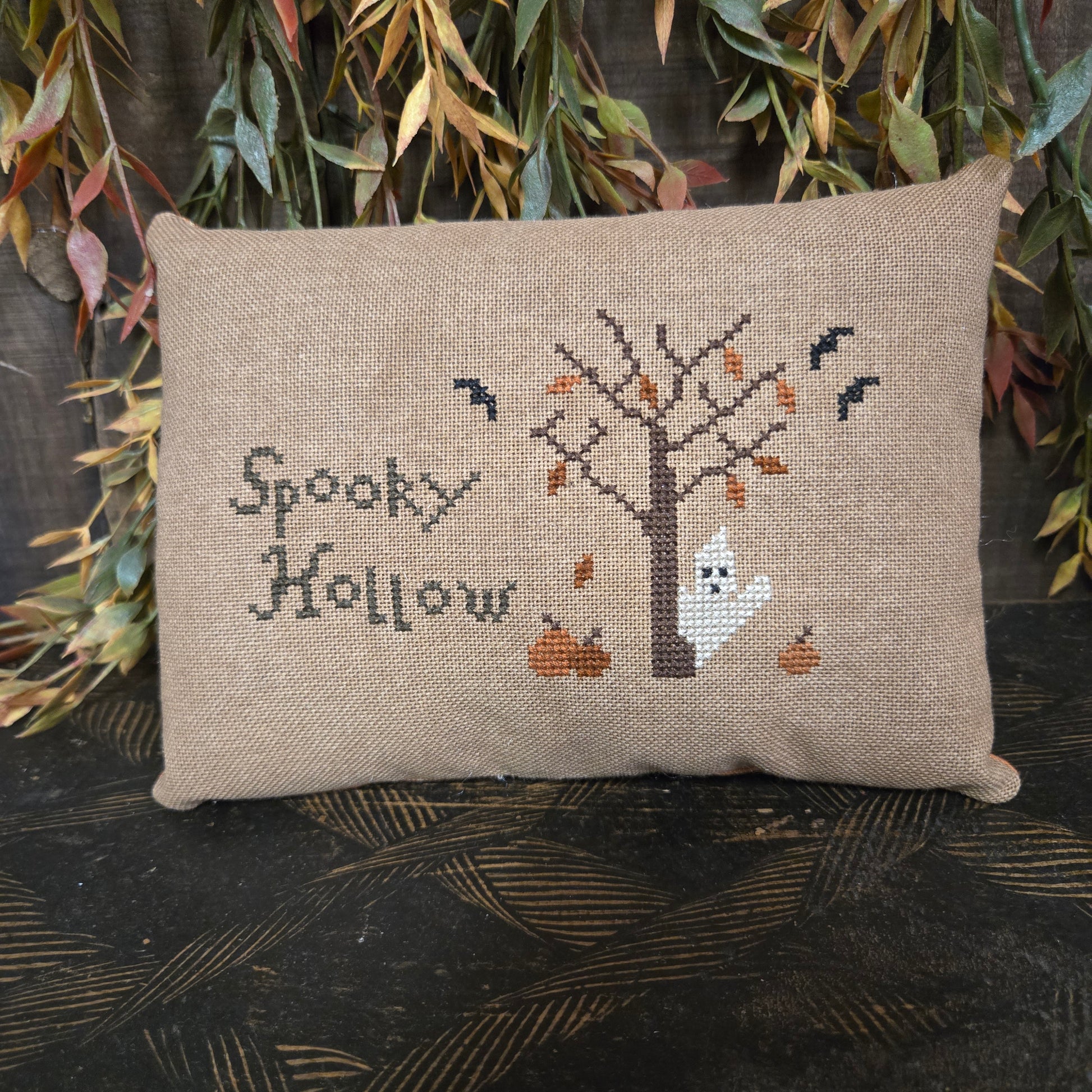 Cross-stitched pillow with ghost design and 'Spooky Hollow' text on a textured surface.