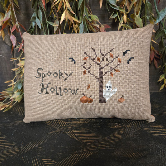 Cross-stitched pillow with ghost design and 'Spooky Hollow' text on a textured surface.