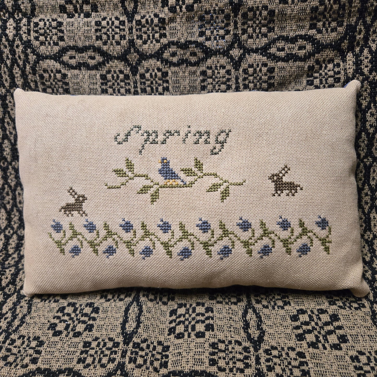 Decorative pillow with cross-stitched design on a patterned fabric background