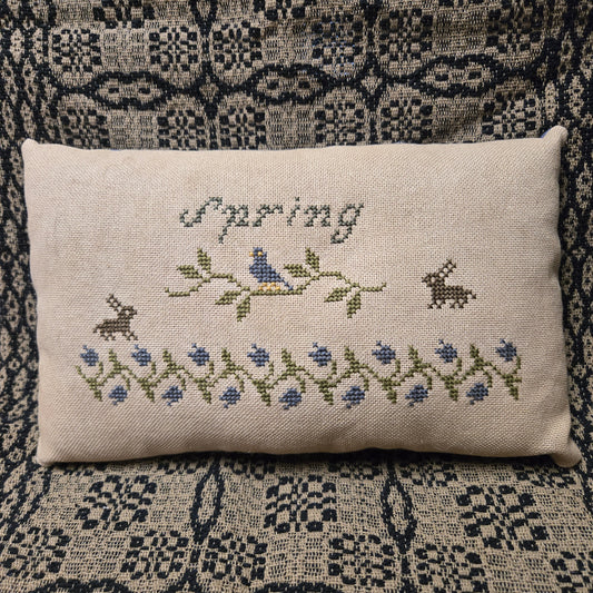 Decorative pillow with cross-stitched design on a patterned fabric background