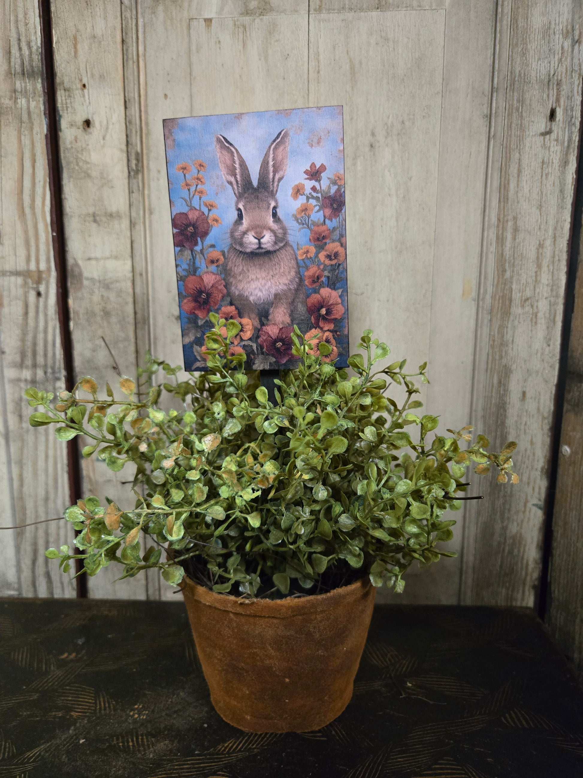 Decorative painting of a rabbit with flowers on on a plant poke in a potted plant.