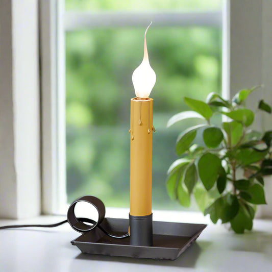 A square pan window light with a smokey black finish, featuring a candle-like bulb glowing on a windowsill.