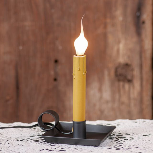 A square pan window light with a smokey black finish, featuring a candle-like bulb glowing on a windowsill.