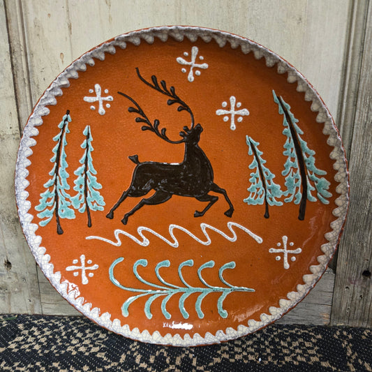 Redware plate of a stag leaping in between trees and snowflakes