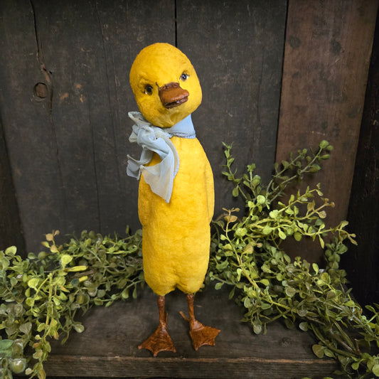 Yellow duck plush toy on a wooden surface with green leaves