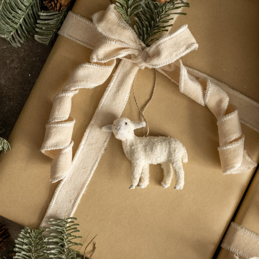 Gift wrapped in brown paper with a white ribbon and sheep ornament, surrounded by greenery.
