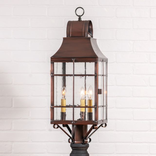 Decorative outdoor lantern with three lit candles against a white brick wall.