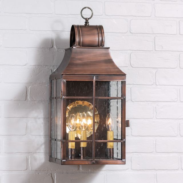 Bronze wall-mounted lantern with glass cover on a white brick wall