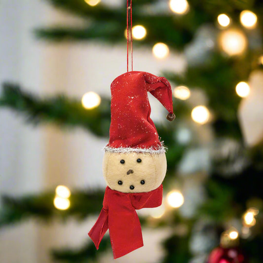 A plush snowman head ornament with a red fabric scarf and stocking cap, hanging from a fabric string.