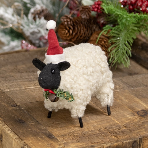 Decorative sheep figurine with a Santa hat and Christmas wreath on a wooden surface with festive background.