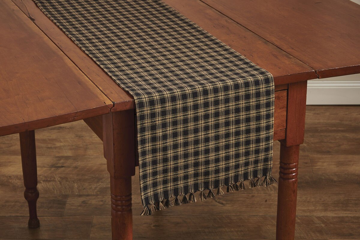 Wooden table with a plaid table runner on a wooden floor.