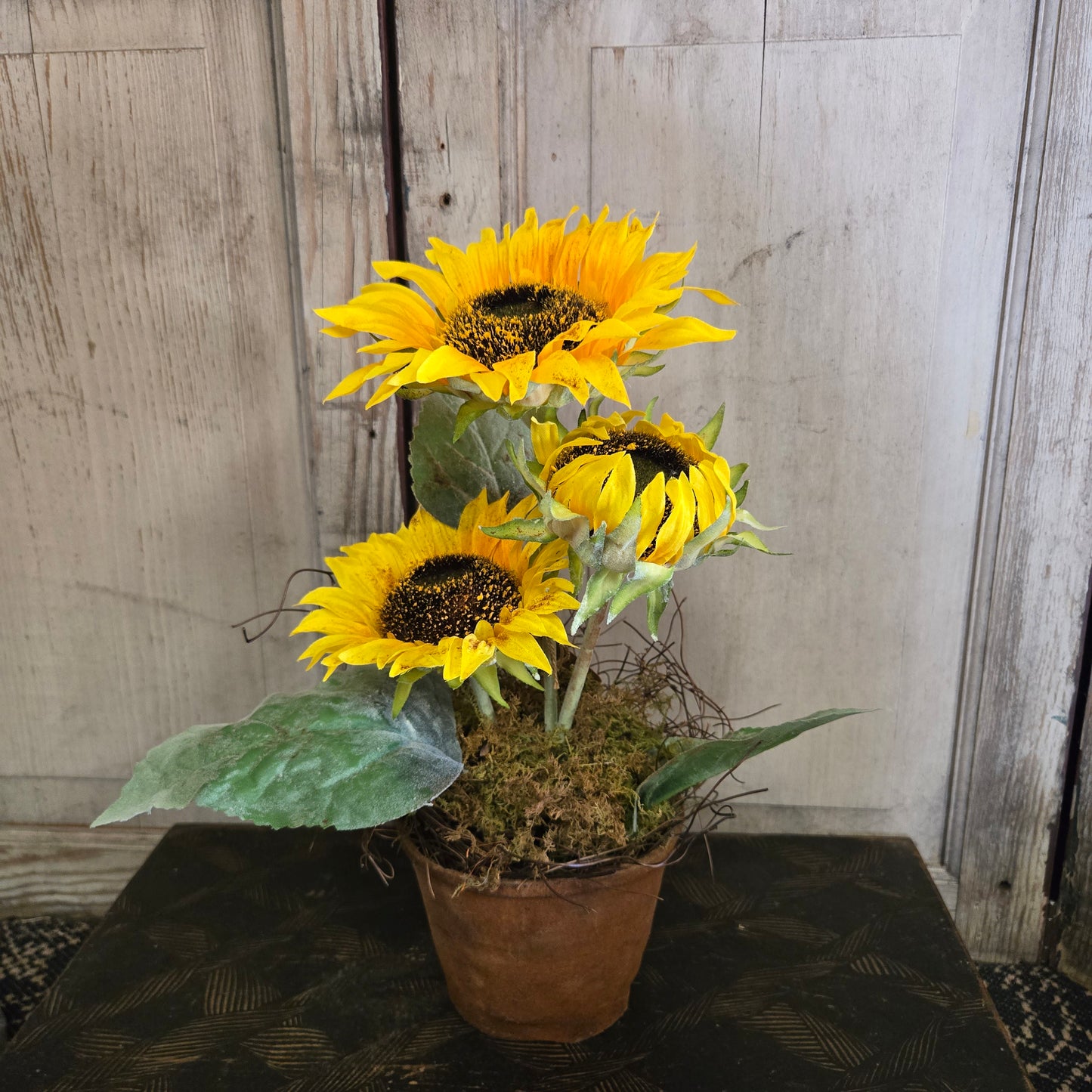 Three sunflowers in a pot on a wooden surface