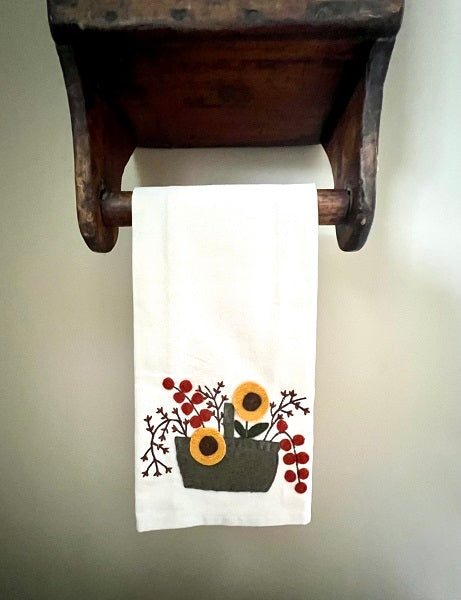 A white hand towel with a sunflower pattern and bittersweet accents, hanging on a wooden towel bar.