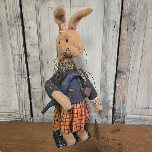 A toy depicting a primitive-style bunny with bendable ears, wearing a plaid skirt and holding a crow.