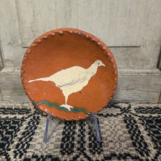 Small round redware plate with a tall white bird standing on grass