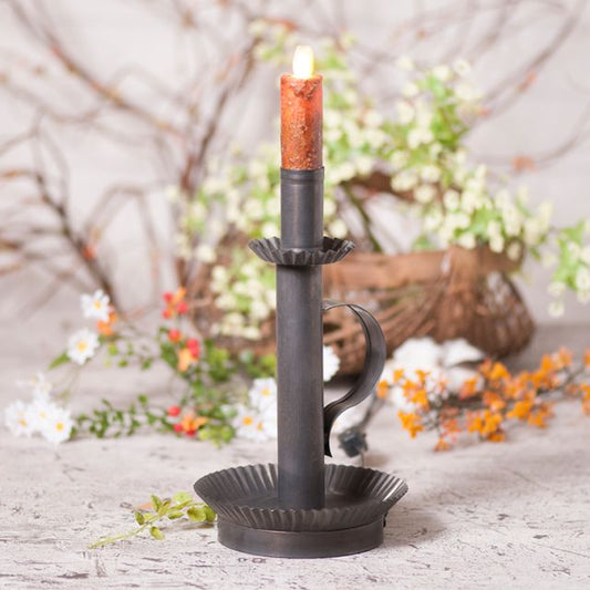 Decorative candle holder with a lit candle on a rustic surface with flowers in the background