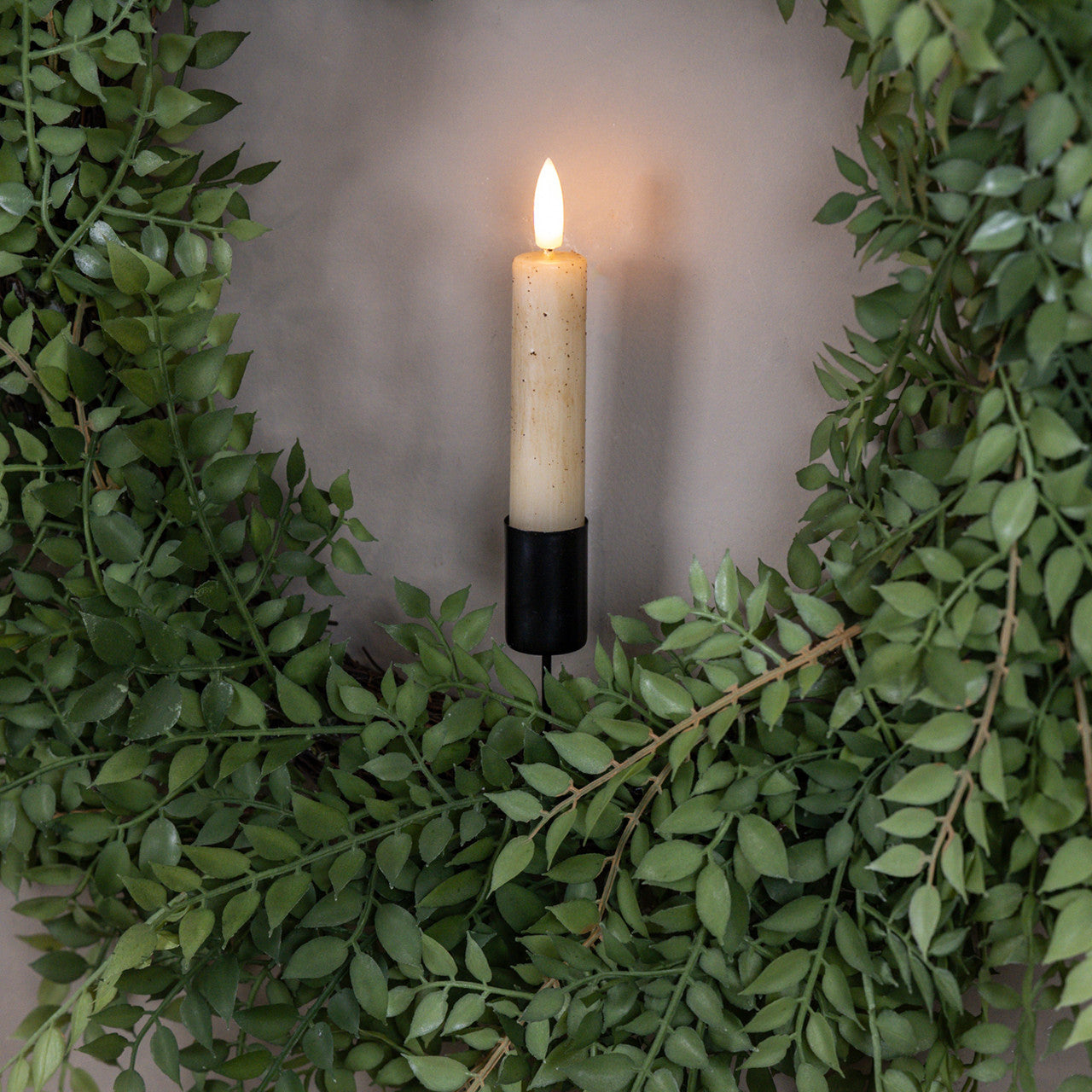 Candle in a decorative wreath with green leaves