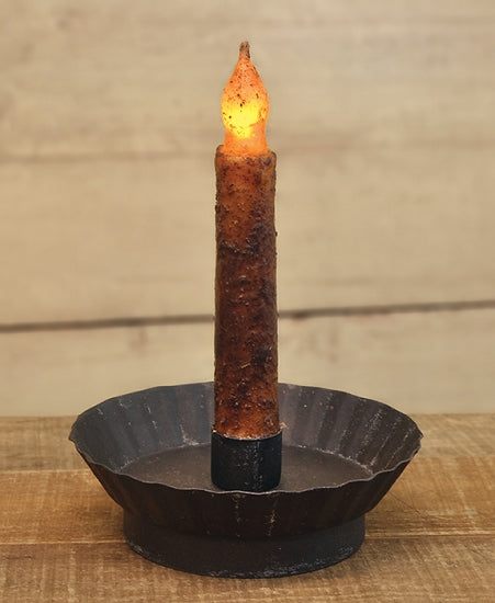 A black metal taper candle holder with a fluted design and a lit candle, set on a wooden surface.