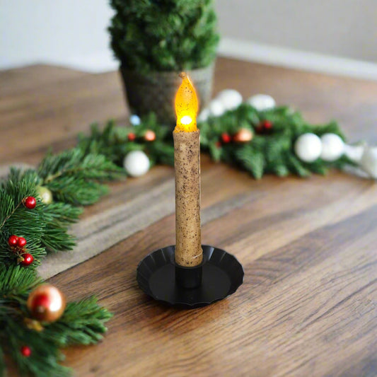 Flickering candle in a decorative holder on a wooden table with Christmas decorations.