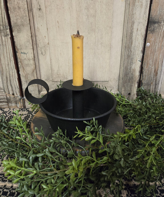 Deep dish candle holder with cream colored candle on a black riser among greenery
