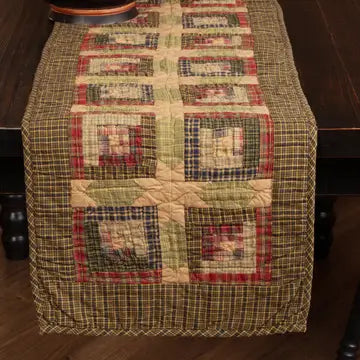 A rustic quilted table runner with a patchwork design in beige, green, red, and brown tones, draped over a dark wooden table.