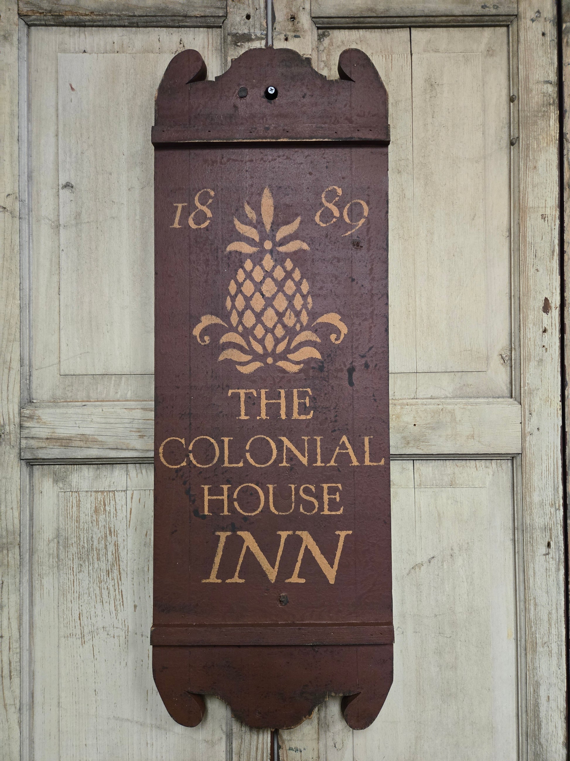 Wooden sign with 'The Colonial House Inn' text and pineapple logo on a wooden background