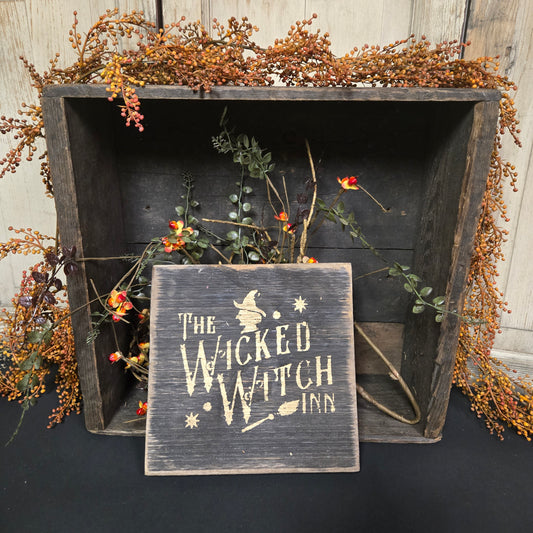 Wooden box with dried flowers and a sign reading 'The Wicked Witch' on a dark background.