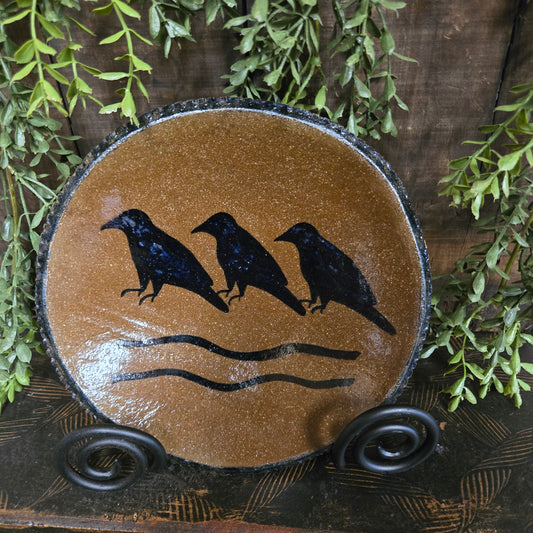Decorative plate with black bird silhouette on a brown background, surrounded by greenery.