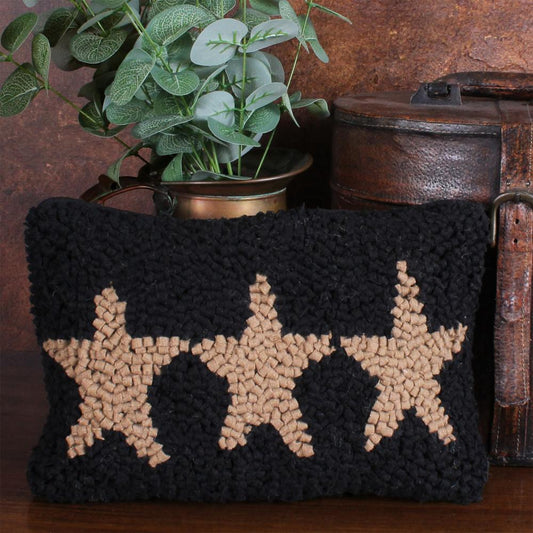 Black pillow with beige star patterns on a wooden surface with a plant in the background
