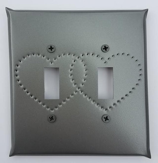 A gray tin double switch plate with heart punch design, featuring two toggle switches.