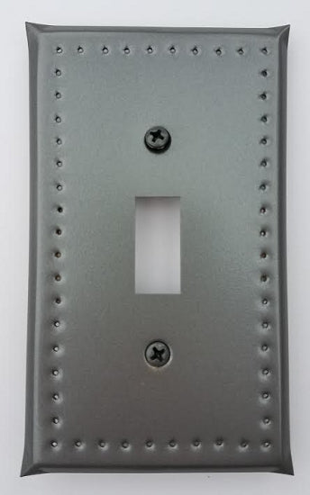 A tin single switch plate border punch with a visible switch cut-out and punched hole design on a gray background. Screws are visible on the top right corner.