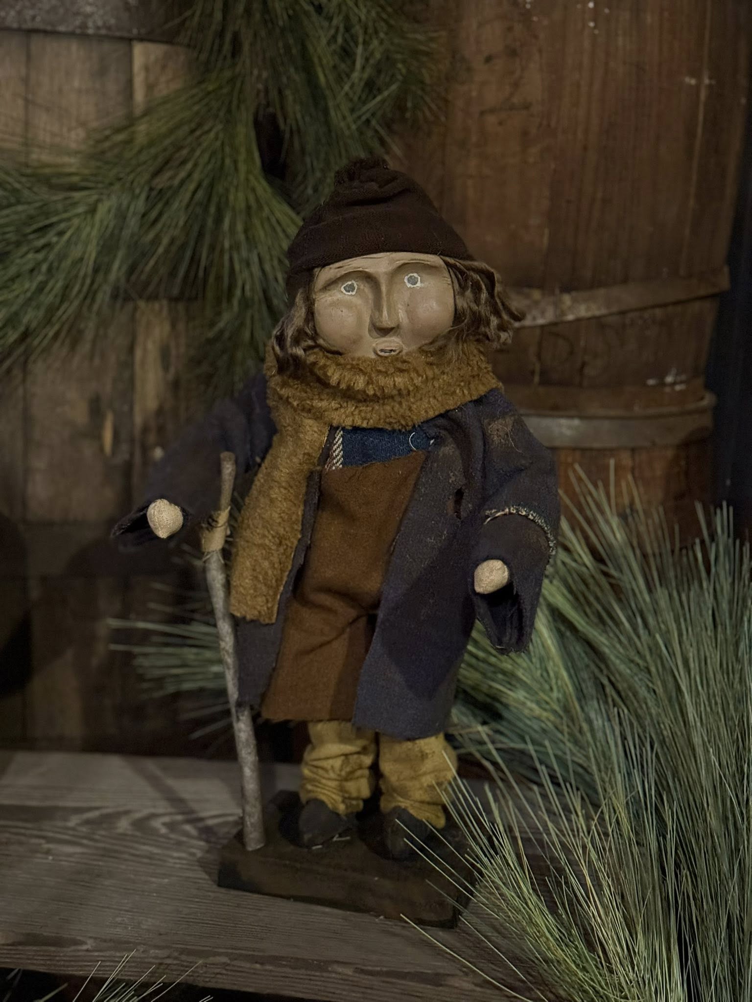 Vintage-style figurine of a person in a coat and hat with a walking stick, set against a rustic wooden background.