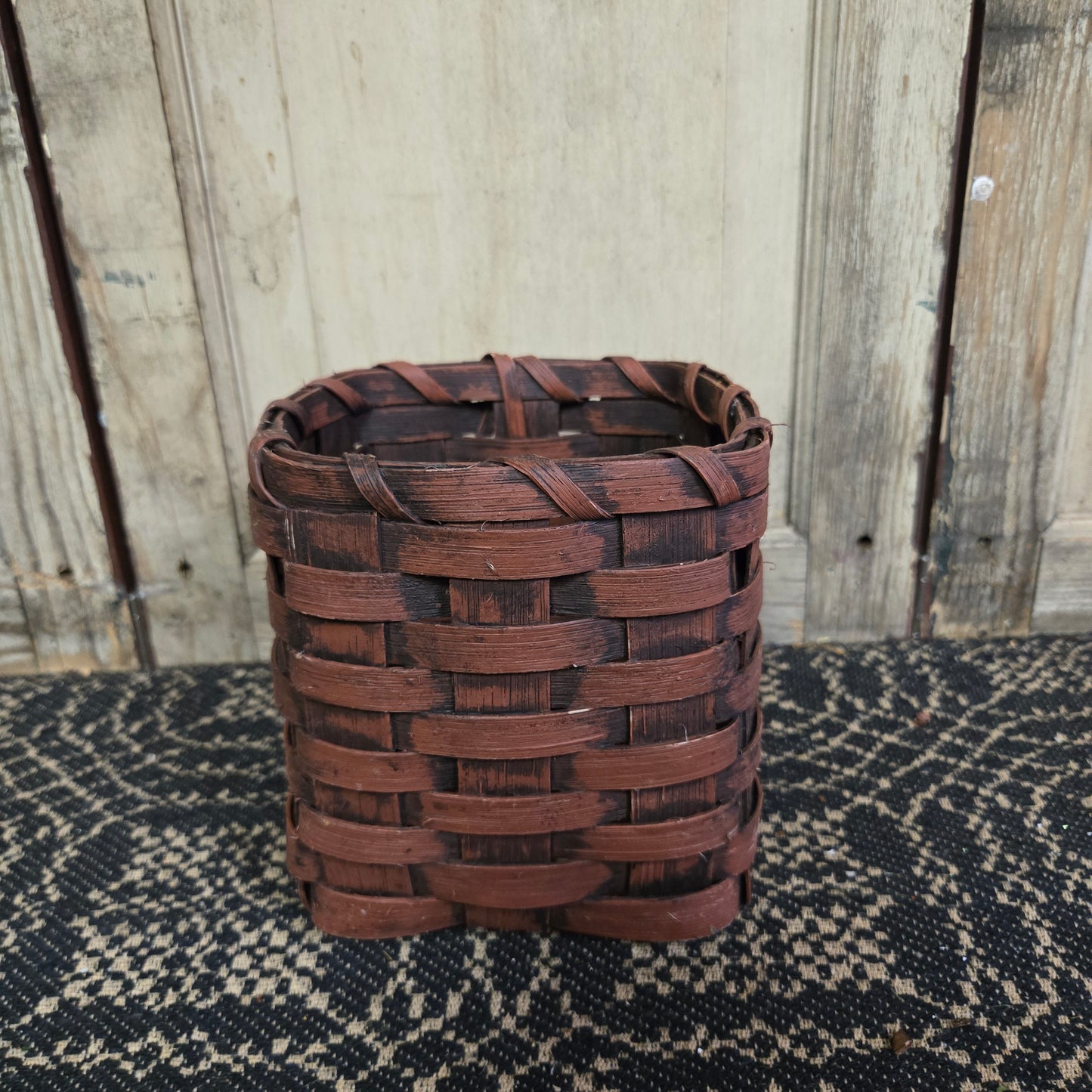 A burgundy wicker tissue box holder placed on a black textured surface against a wooden backdrop.