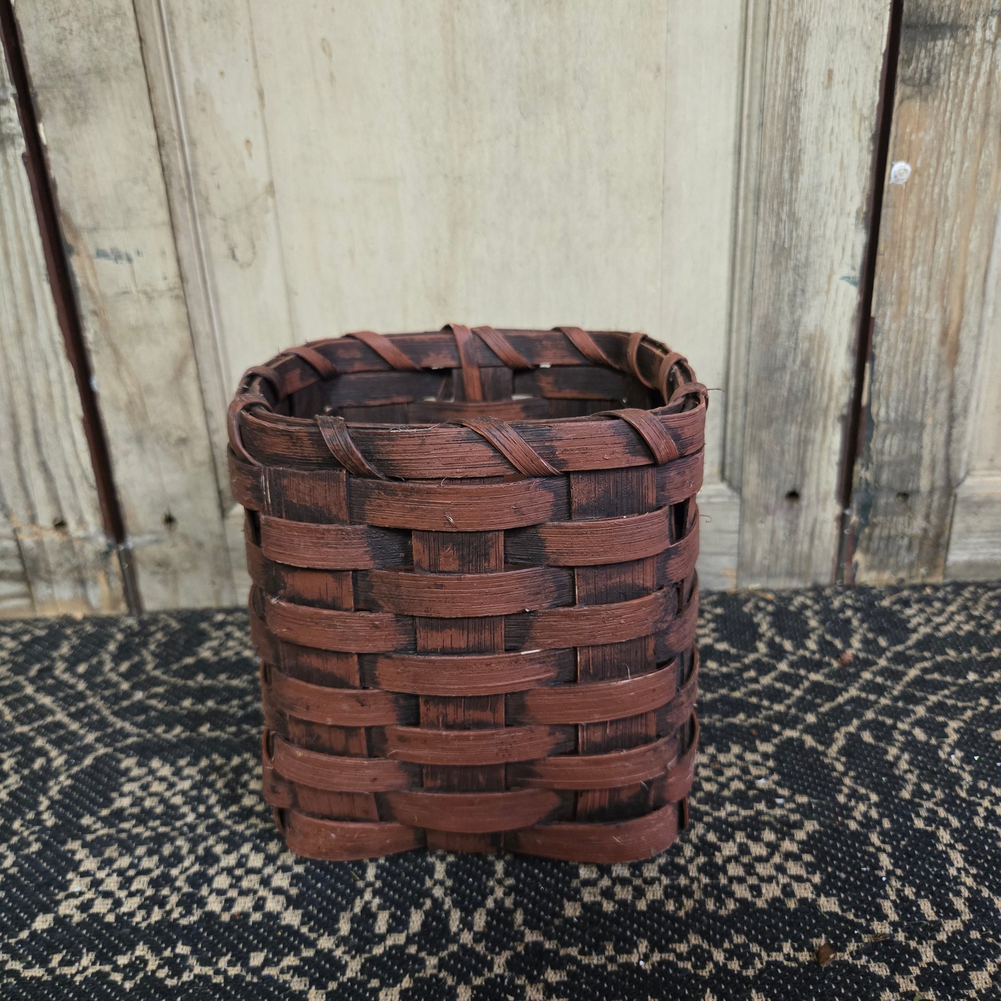 A burgundy wicker tissue box holder placed on a black textured surface against a wooden backdrop.