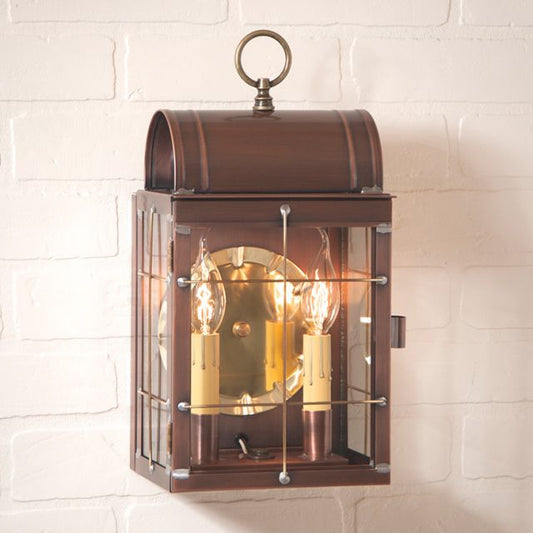 Antique copper wall lantern with clear glass and brass-tone hardware, featuring a 2-light bulb holder, mounted on a white brick wall.
