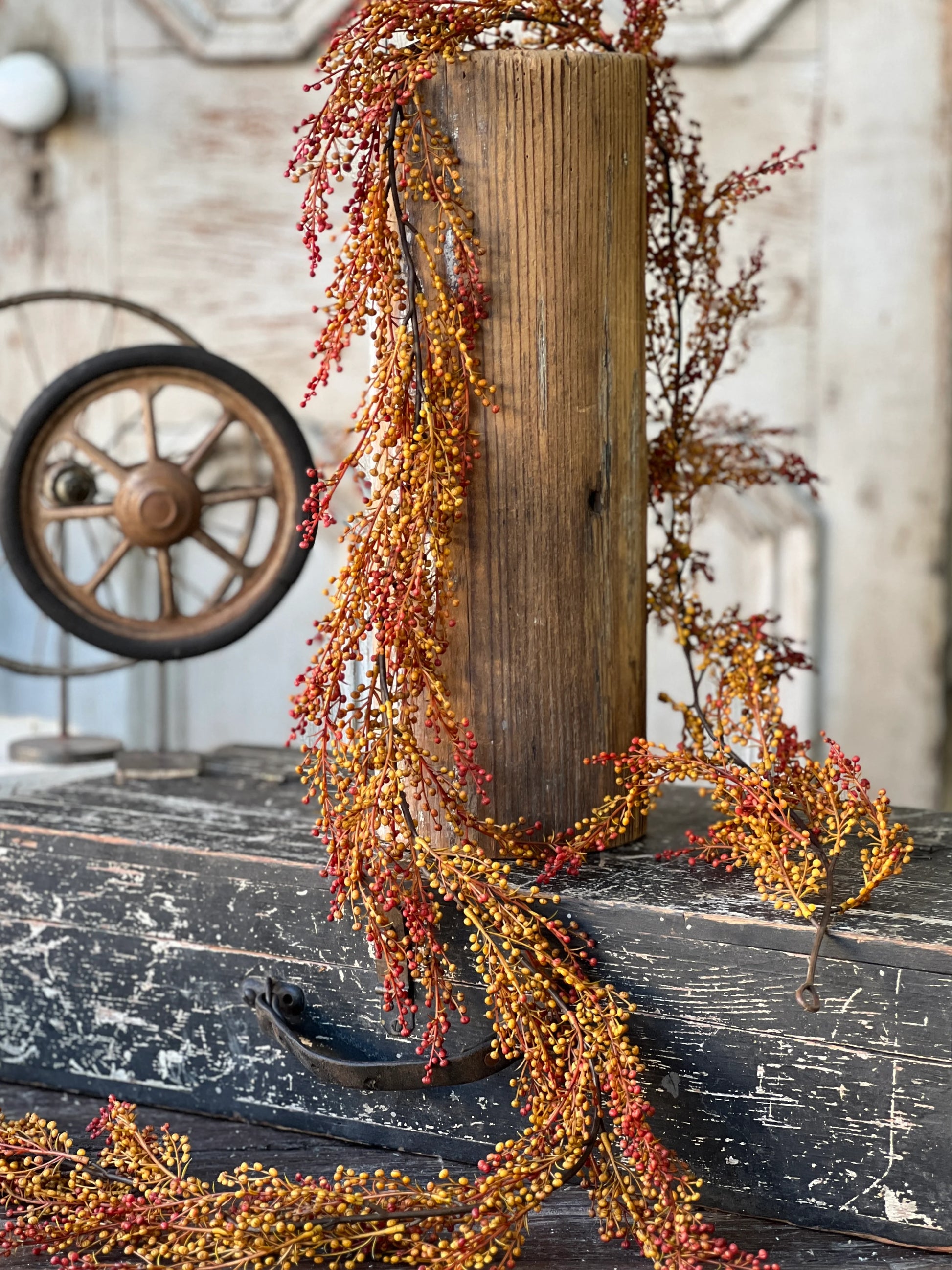 A garland of torchlight berries with shades of orange and yellow, displayed draping over a rustic wooden object.